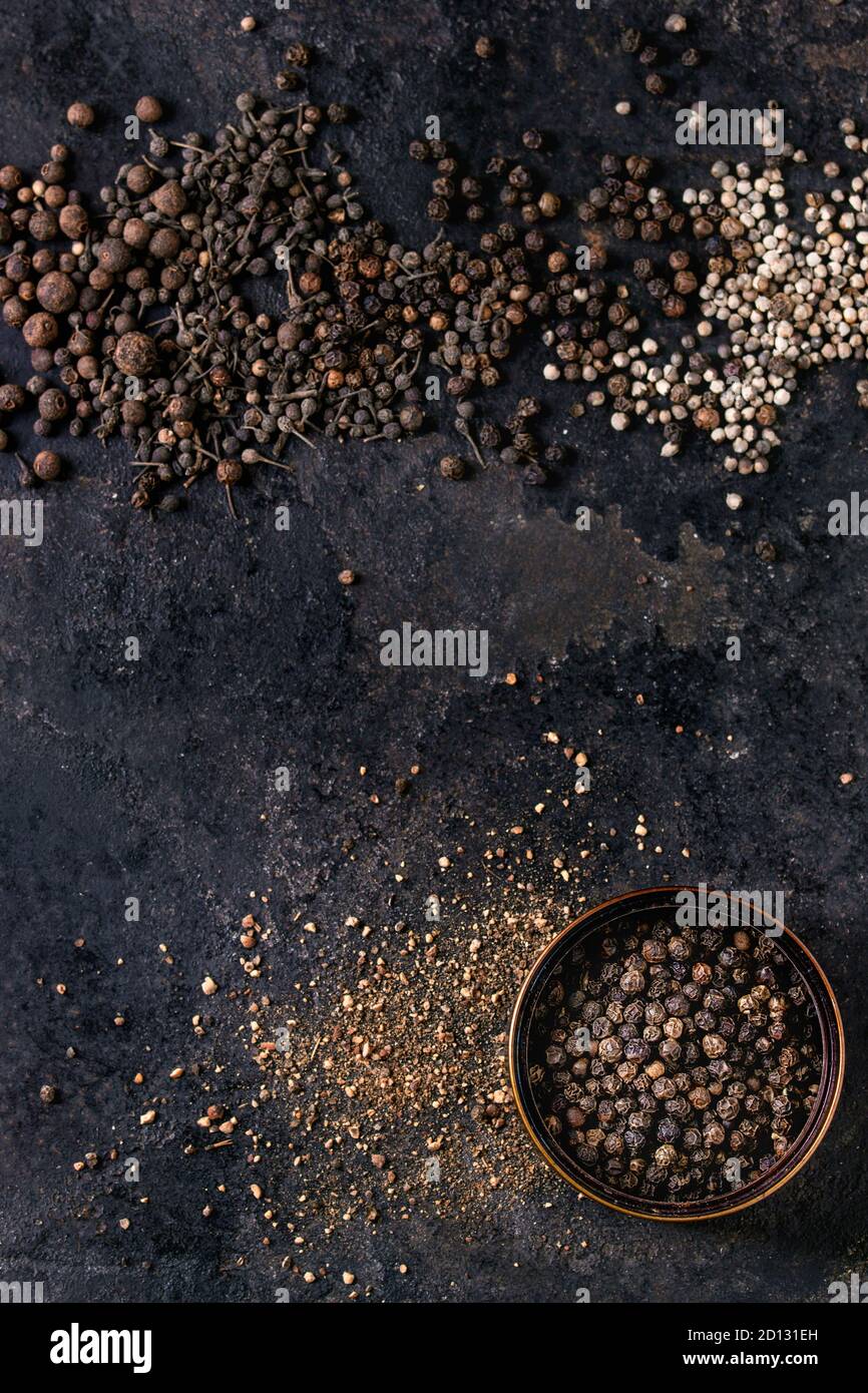 Variety of different black peppers allspice, pimento, monks pepper, peppercorns and ground powder in tin can over old black iron texture surface. Top Stock Photo