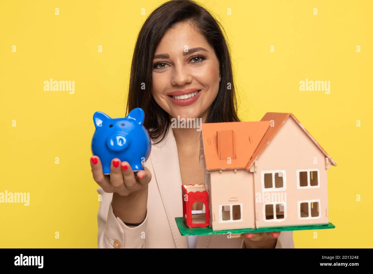 young businesswoman in pink suit presenting piggy bank and house model ...