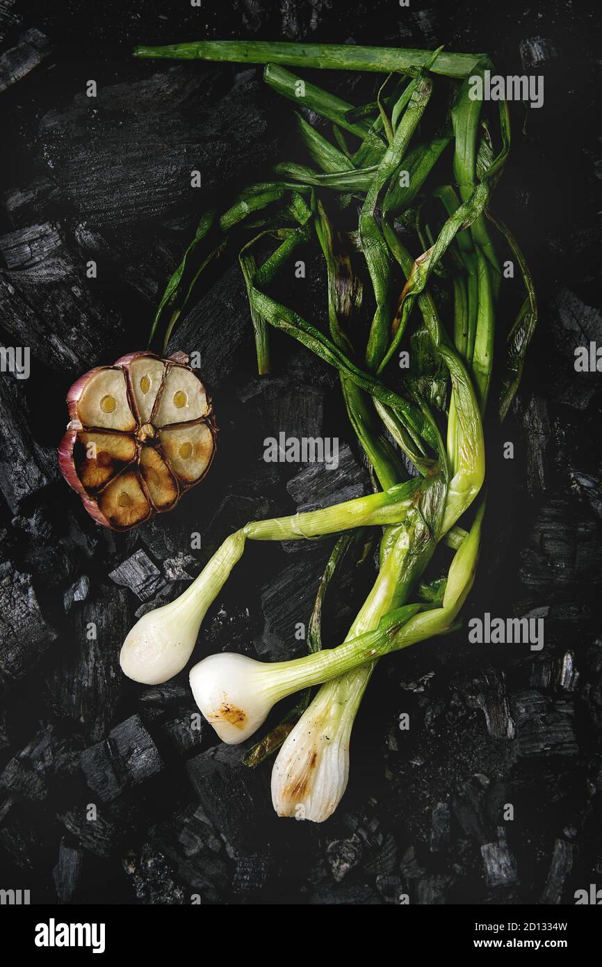 Grilled vegetables spring onion and garlic over black charcoal. Top