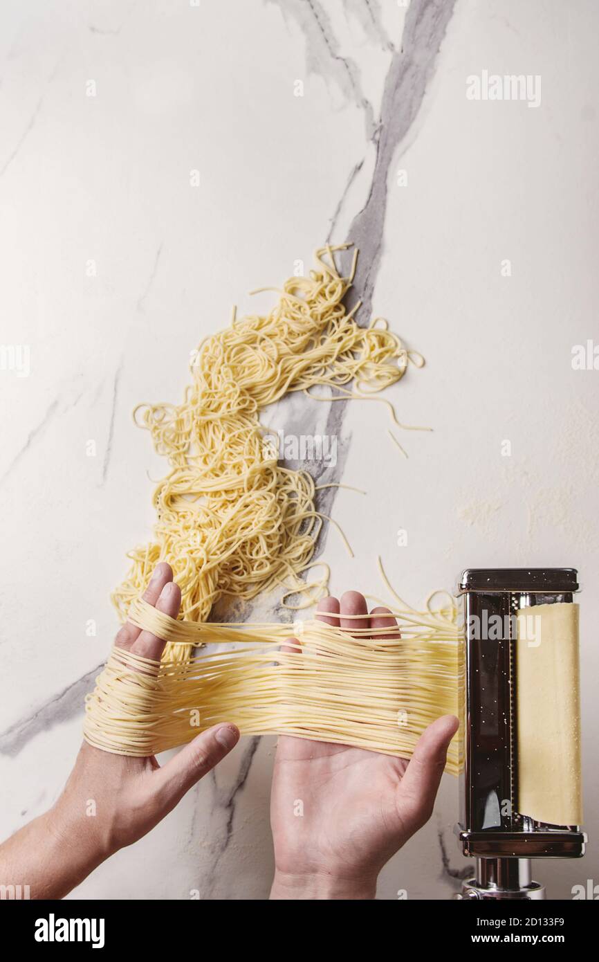 https://c8.alamy.com/comp/2D133F9/rolled-dough-for-homemade-italian-uncooked-pasta-spaghetti-from-pasta-machine-maker-in-hands-with-semolina-flour-over-white-marble-texture-background-2D133F9.jpg