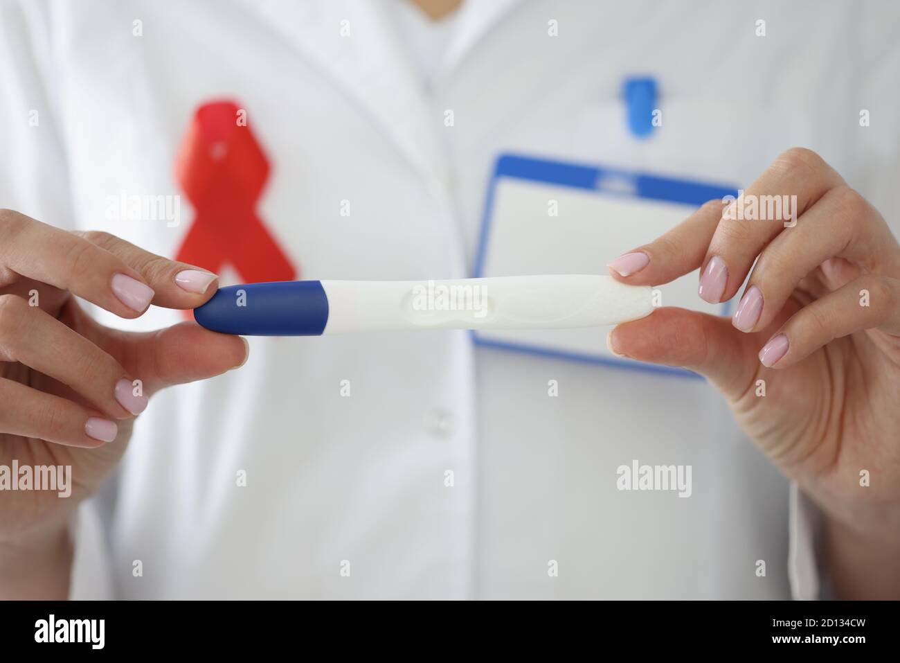 Doctor's hands with red ribbon on his chest hold pregnancy test closeup