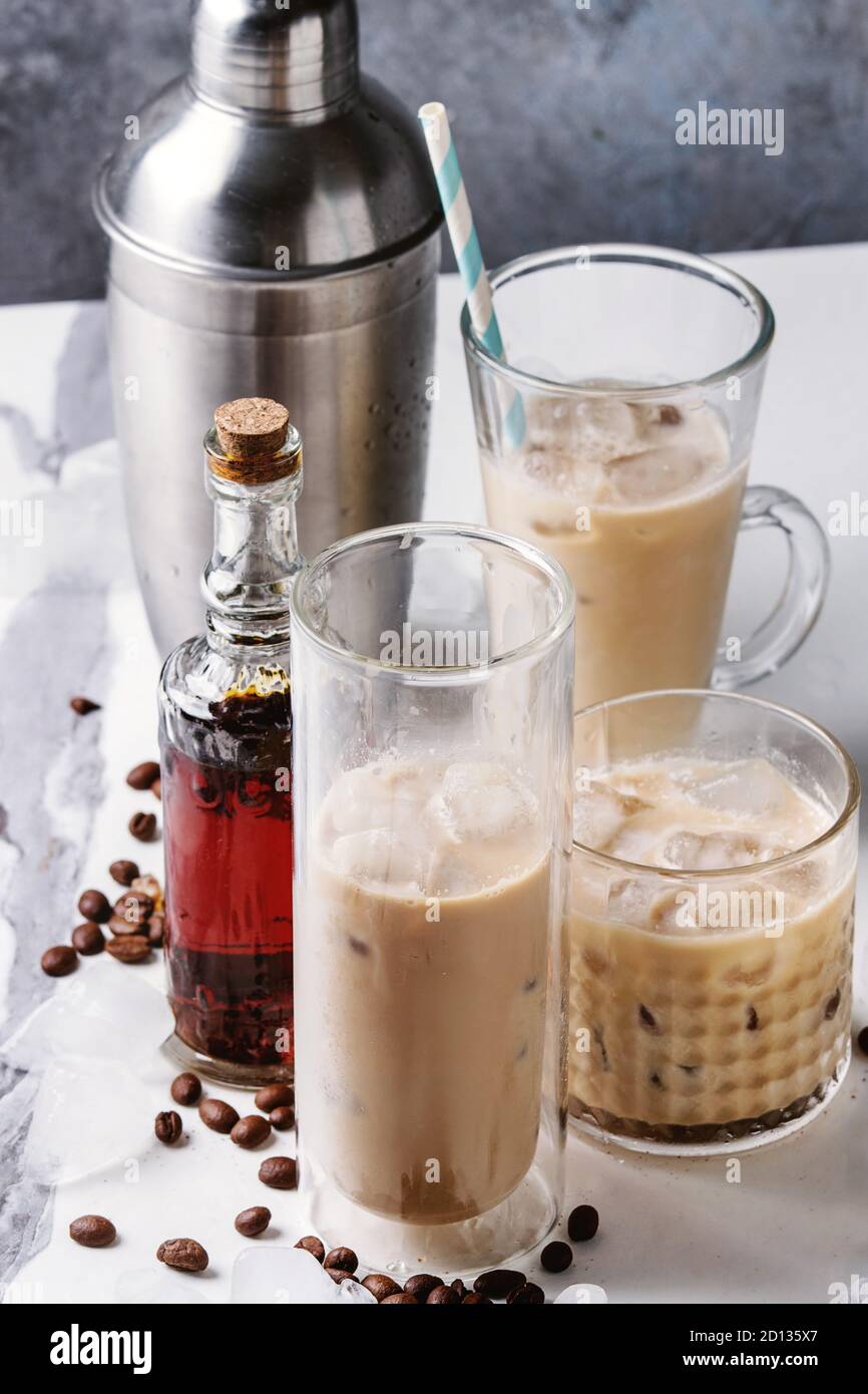 https://c8.alamy.com/comp/2D135X7/iced-coffee-cocktail-or-frappe-with-ice-cubes-and-cream-in-different-glasses-with-silver-shaker-bottle-of-rum-coffee-beans-around-on-white-marble-ta-2D135X7.jpg
