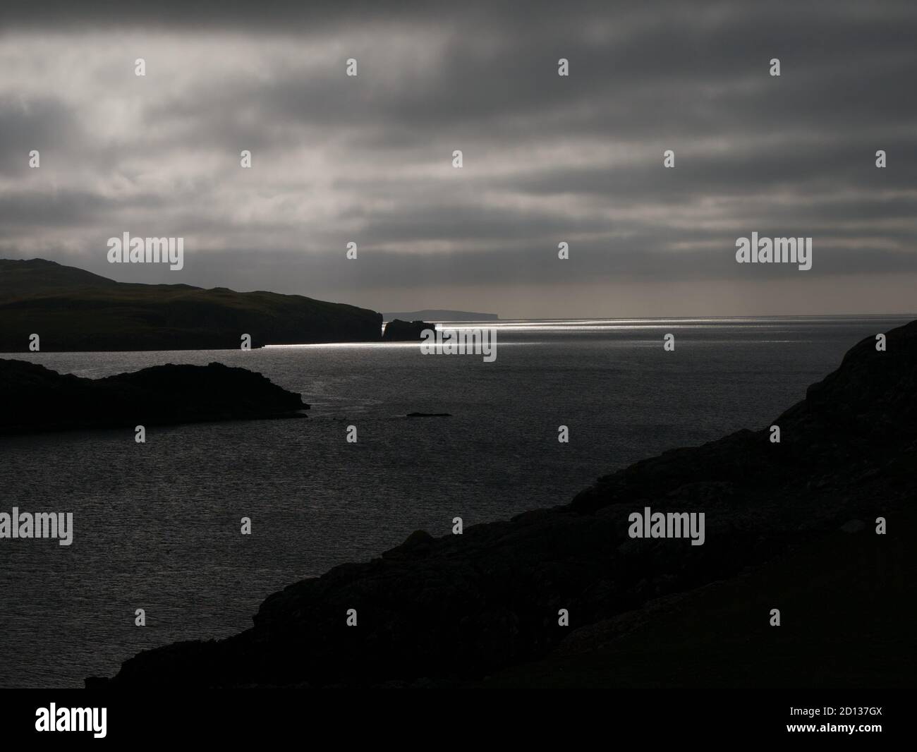 In black and white, a moody, threatening view of sunlight on the water across Magnus Bay from hillside at Islesburgh near Mavis Grind,  Shetland, UK. Stock Photo