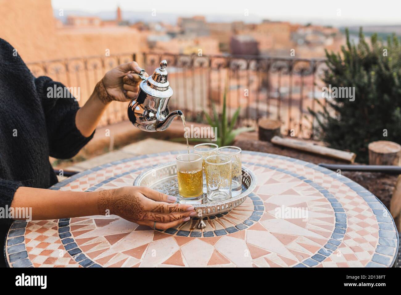 Woman hand pouring traditional moroccan mint tea in glasses. Vintage silver tray and teapot. Round mosaic table. Morocco hospitality. Stock Photo