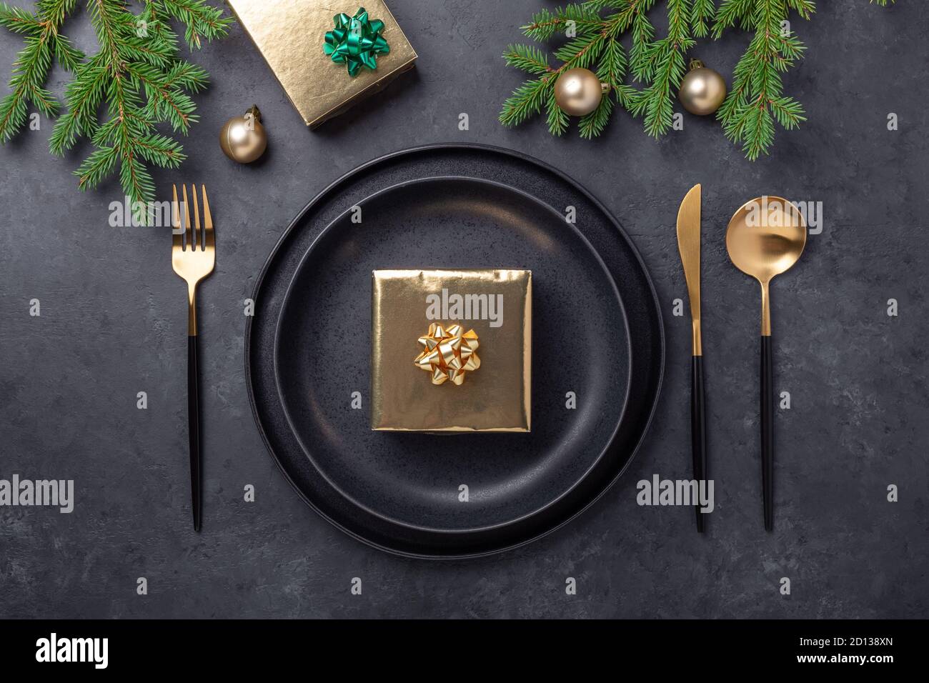 Christmas table setting. Black ceramic plate with golden gift box, fir tree  branch and accessories on stone background. Gold decoration - Image Stock  Photo - Alamy