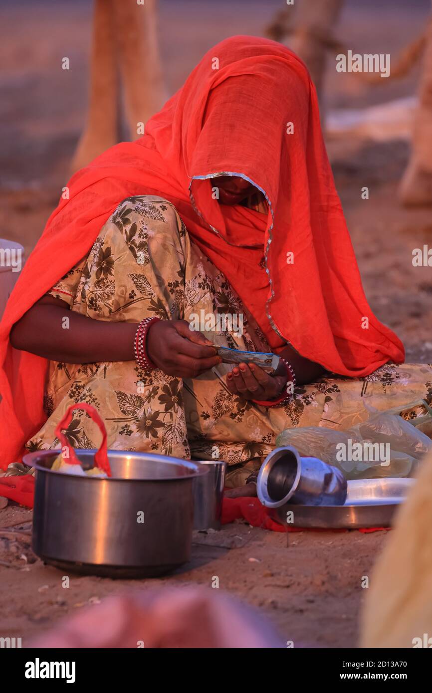 A women wearing an orange traditional Rajasthani dress covering her face and siting on ground at Pushkar,Rajasthan India on 18 November 2018 Stock Photo