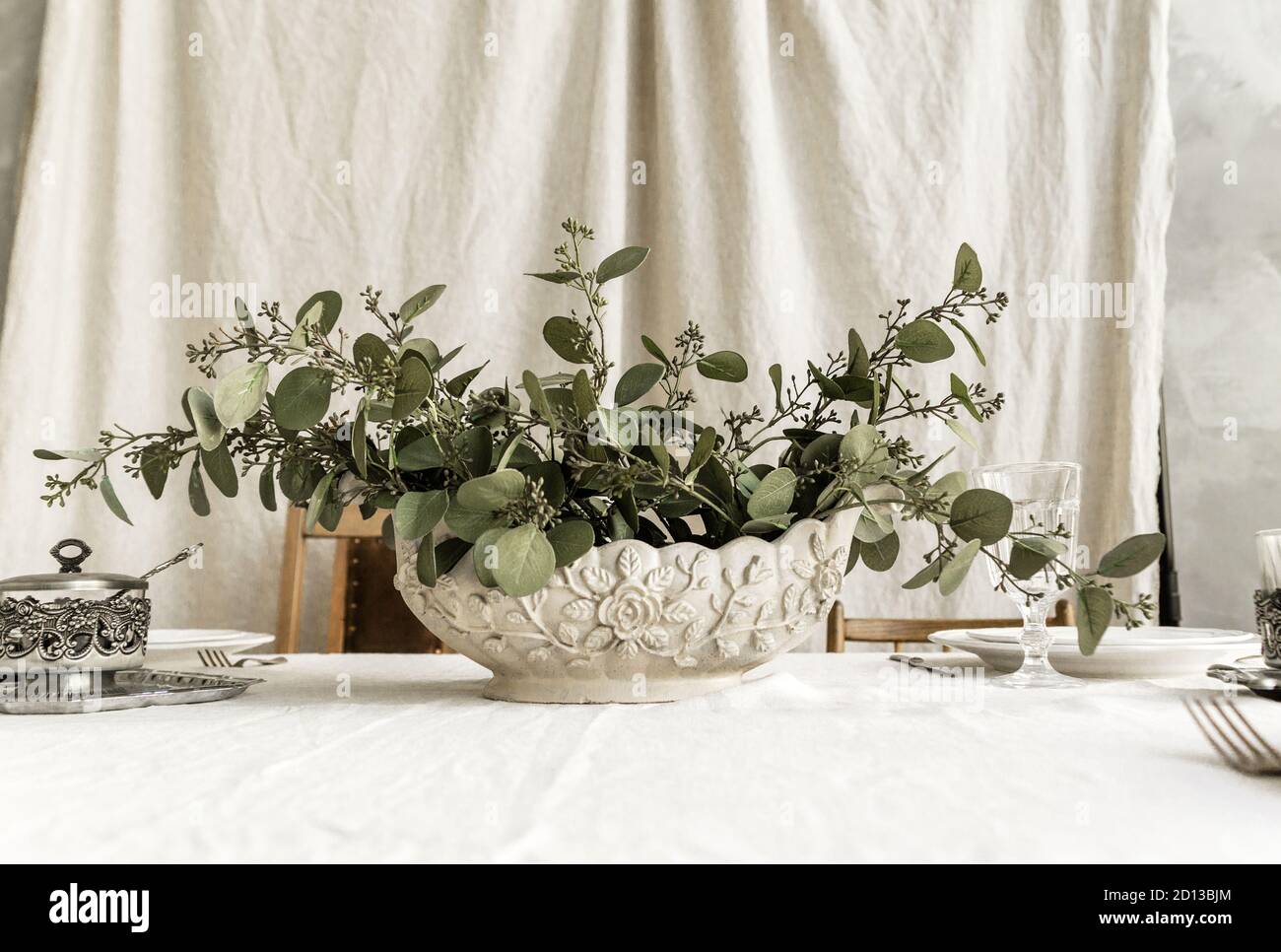 Decorated boho table. The table is covered with a tablecloth, on which there are elegant plates and glasses, a vase with a green plant Stock Photo