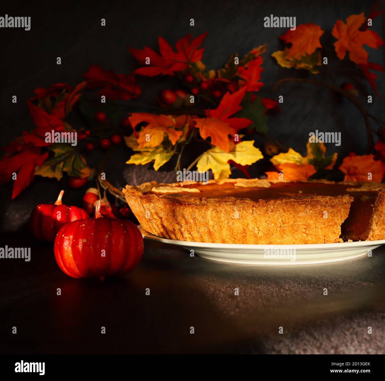 Closeup of Pumpkin Pie Crust on White Plate shot during Sunny Day. Baked Autumn Food with Small Artificial Decorative Pumpkin. Stock Photo