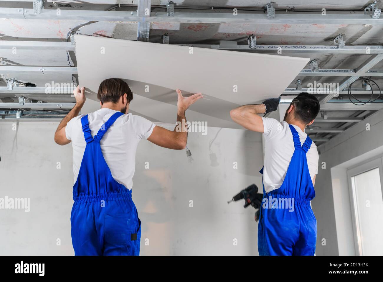 Two builders are making a plasterboard ceiling. They use a drill and