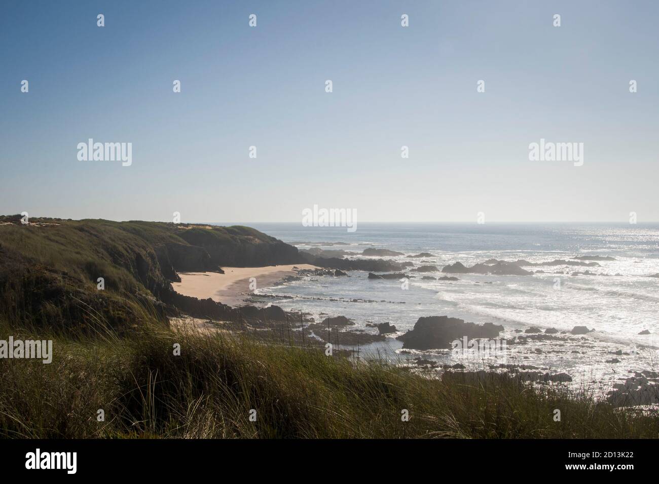 Beach landscape line with wave lines coming ashore and cliffs entering the sand, under a blue sky and sunny day Stock Photo