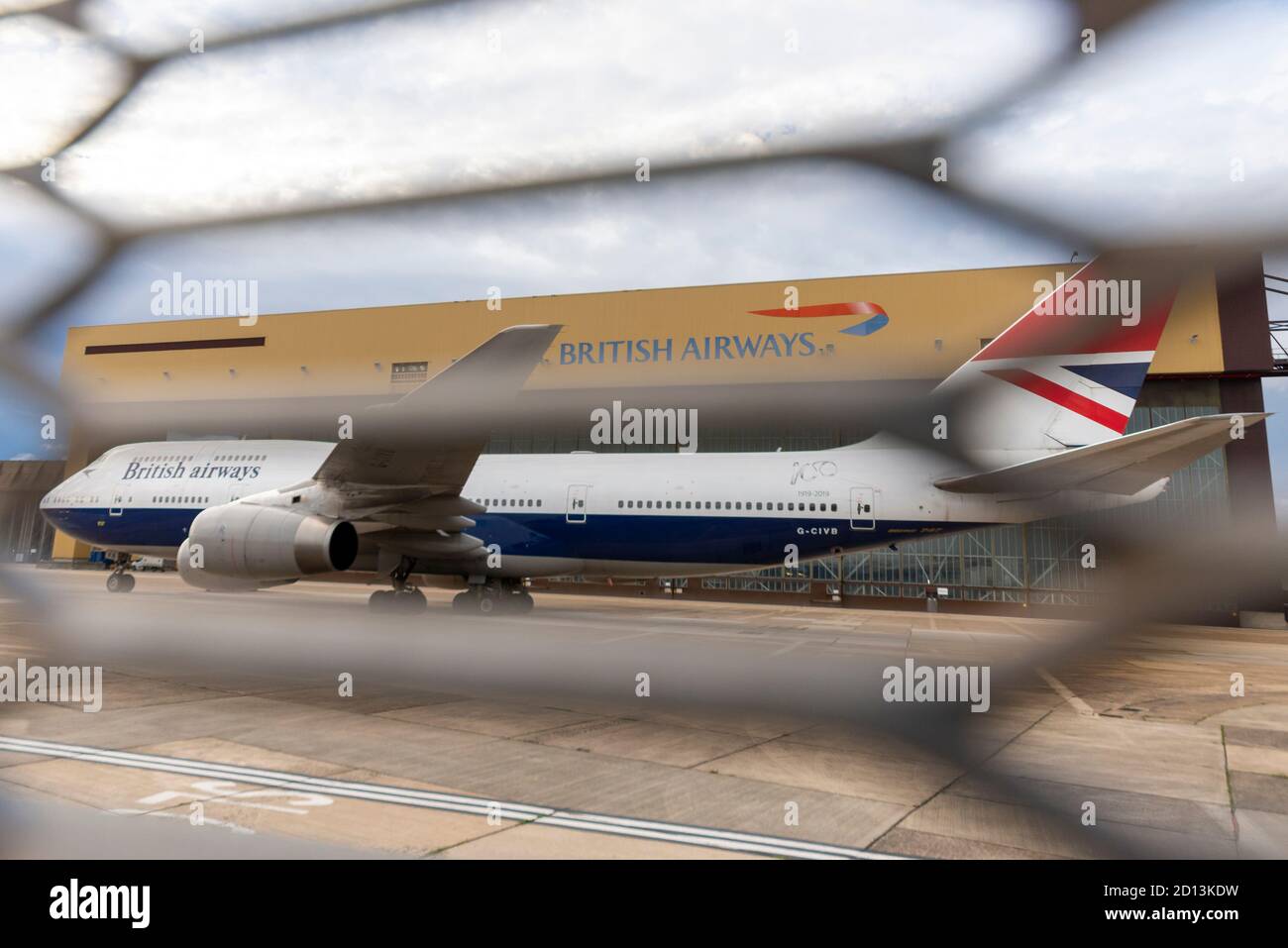 British Airways Boeing 747 Jumbo Jet plane in classic centenary scheme behind fence. Grounded and retired due to COVID-19. Maintenance hangar Stock Photo