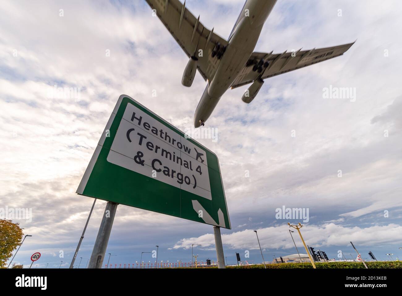 Sign for Heathrow Airport, London, UK, Terminal 4 and cargo, with a jet airliner plane landing, over A30 road. Evening arrival over local sign Stock Photo