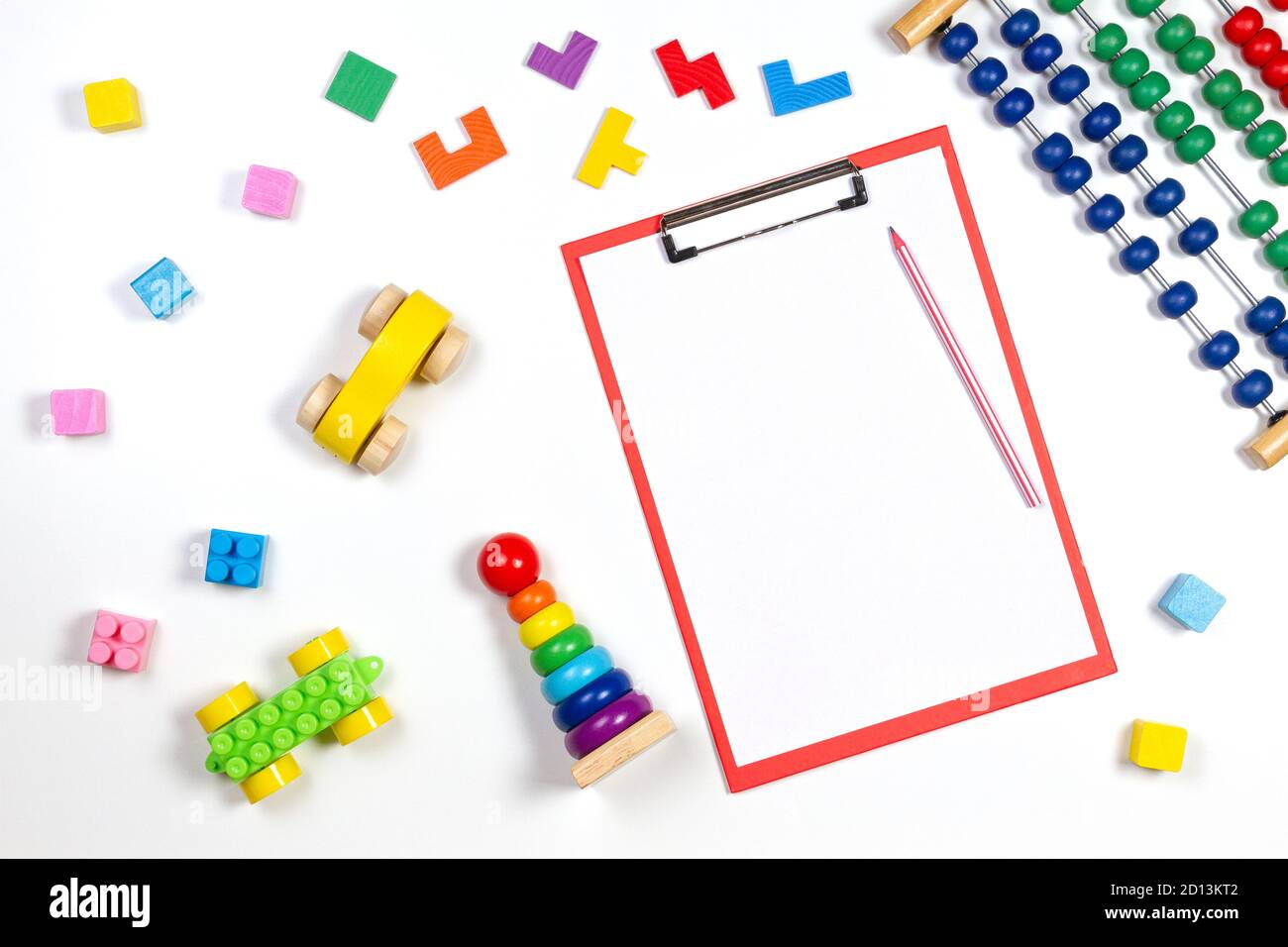 Colorful baby kid toys and red clipboard with blank sheet of paper on white background. Top view Stock Photo