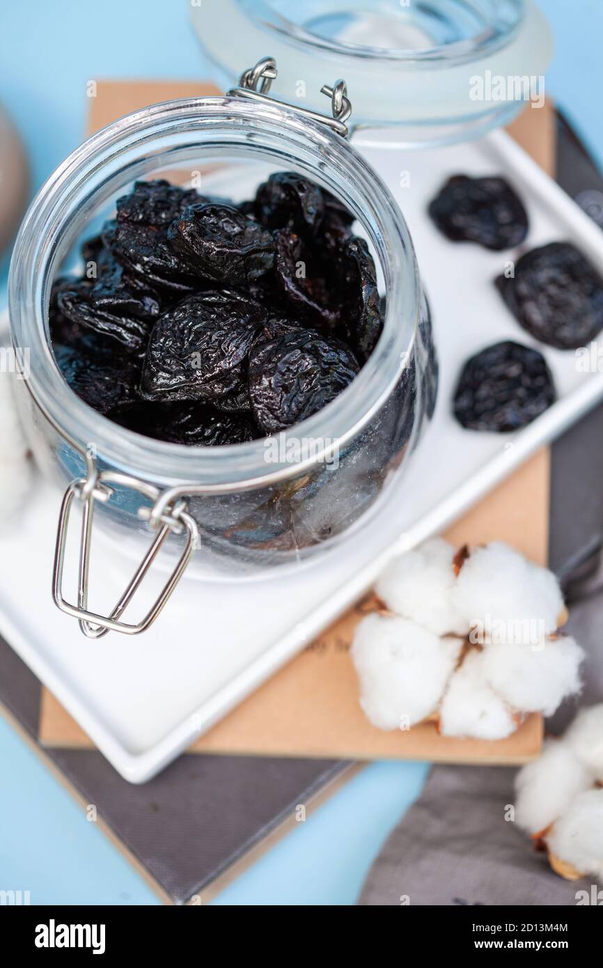 A handful of prunes in a glass jar on a white stand on a blue background. Food photo. Stock Photo