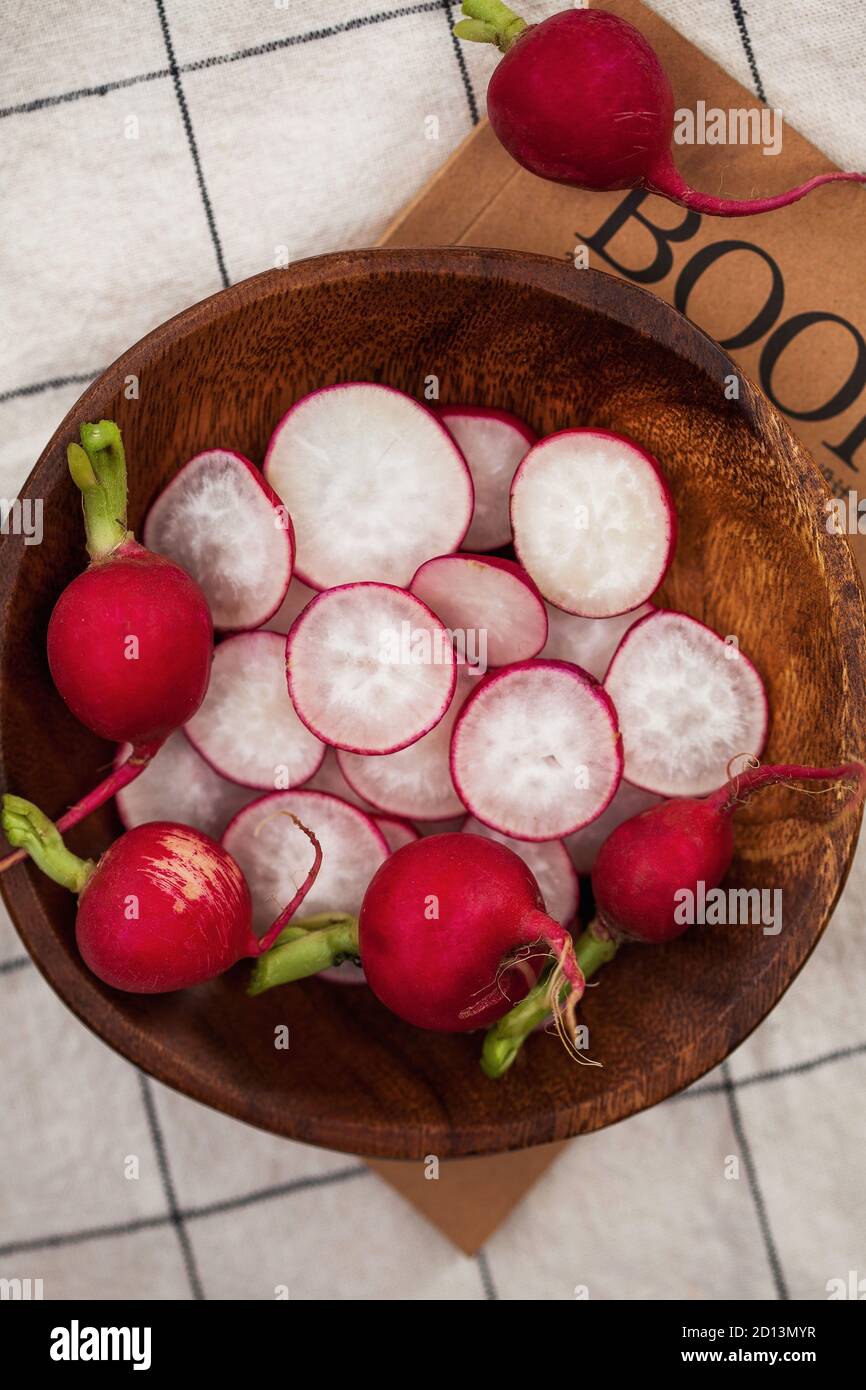 Red radish whole and cut into slices on a wooden plate against a checkered tablecloth. Food photo for ecomarket. Stock Photo