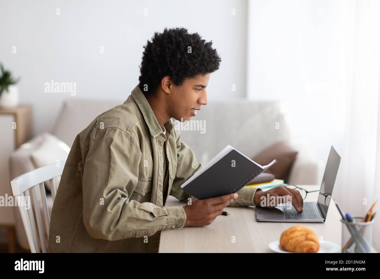 Remote education. Black teenage student with notebook participating in web conference, listening to lecture on webcam Stock Photo