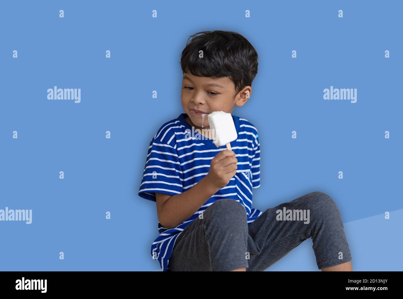 Little Thai boy eating white chocolate Ice cream Isolated over blue background Stock Photo