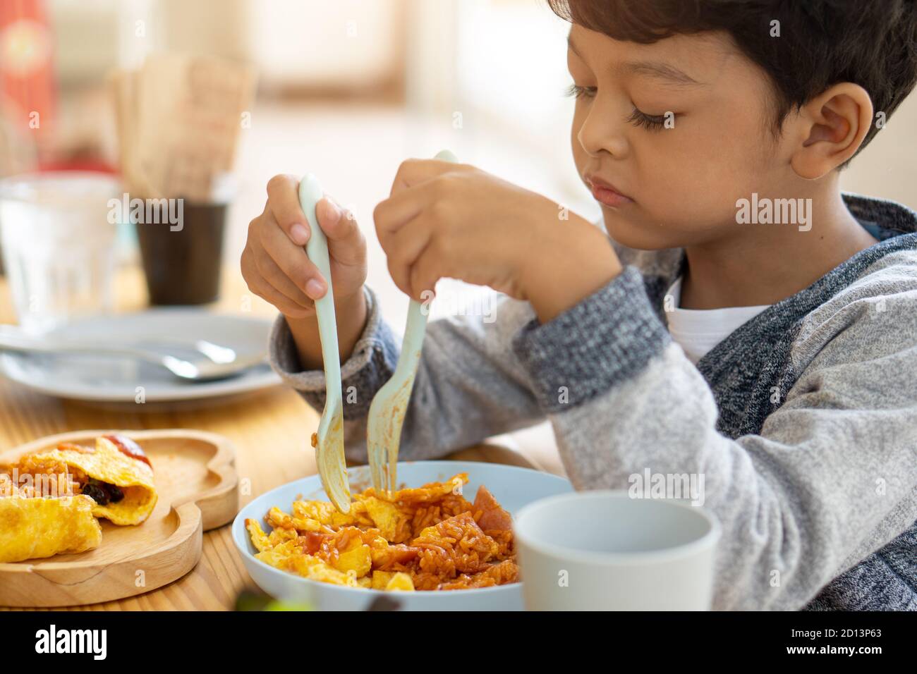 The child eats an omelet wrapped in fried rice with bacon sauce inside. Stock Photo