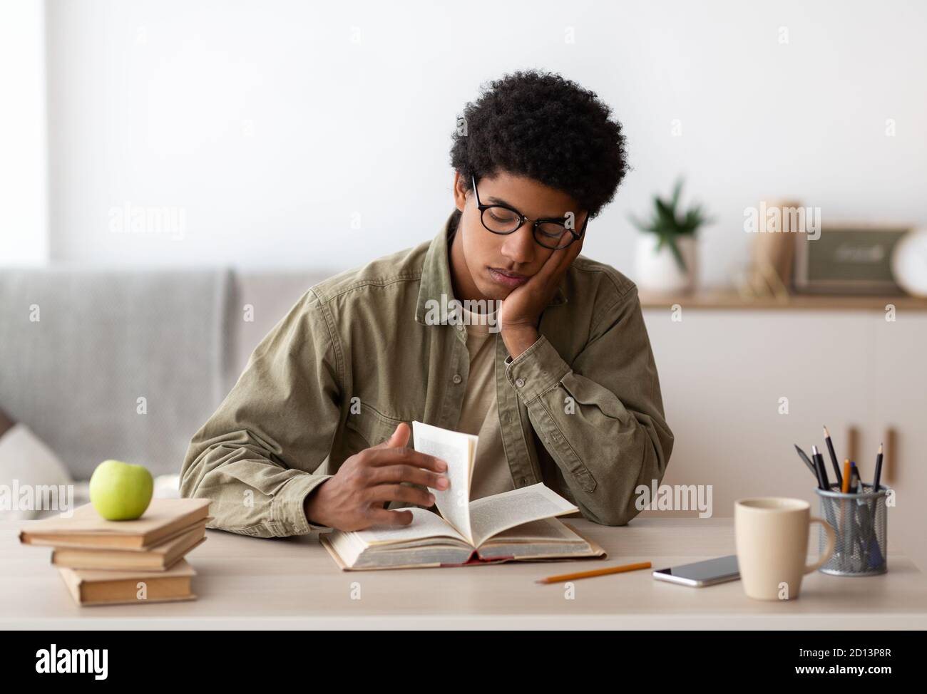 Bored African American teenager reading textbook, getting ready for complicated exam at home Stock Photo