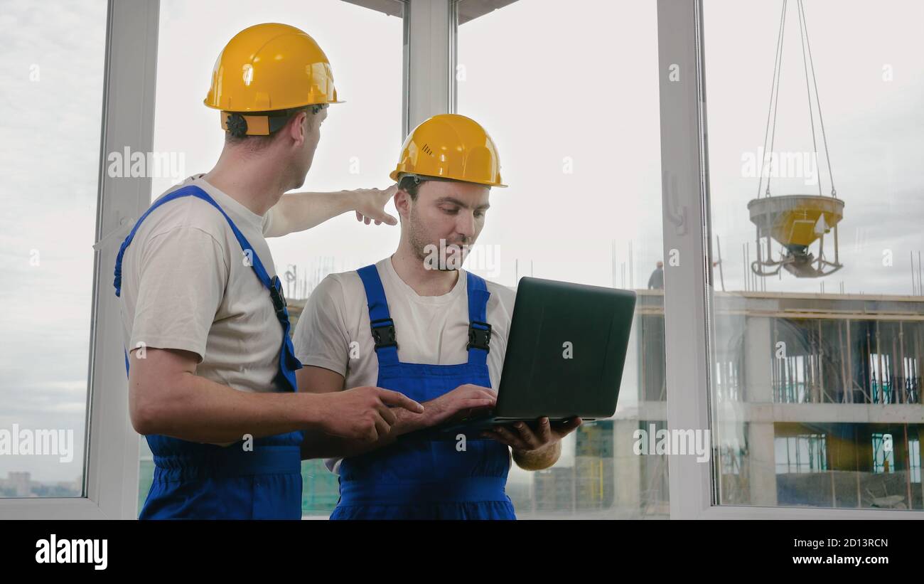 Two builders wearing protective helmets working on a laptop. Stock Photo