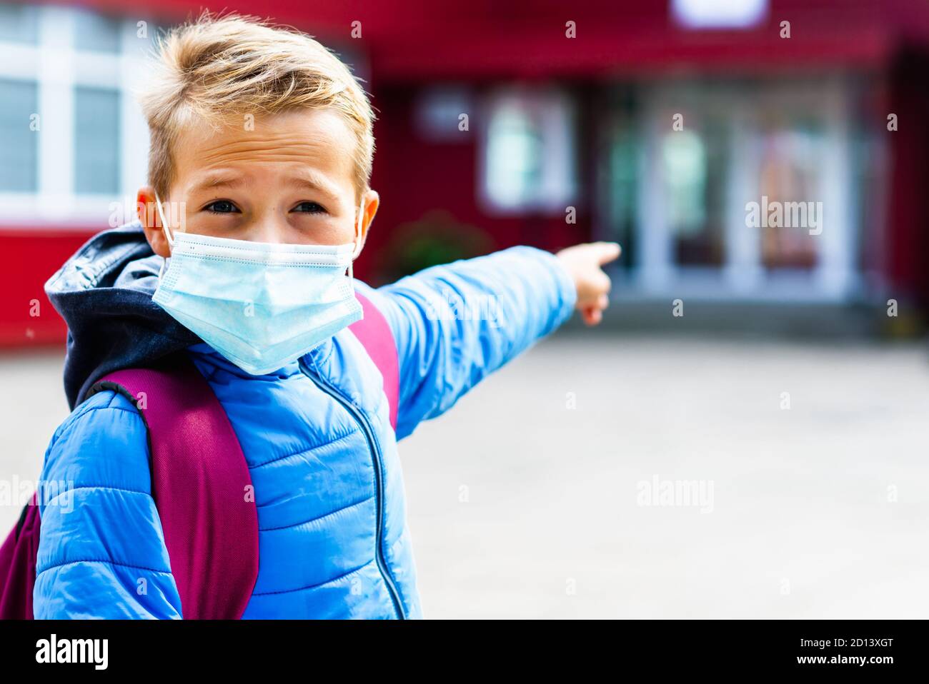 Close up image Attractive schoolboy in protective mask standing outdoor excited child points finger at school Back to school. epidemic influenza and c Stock Photo