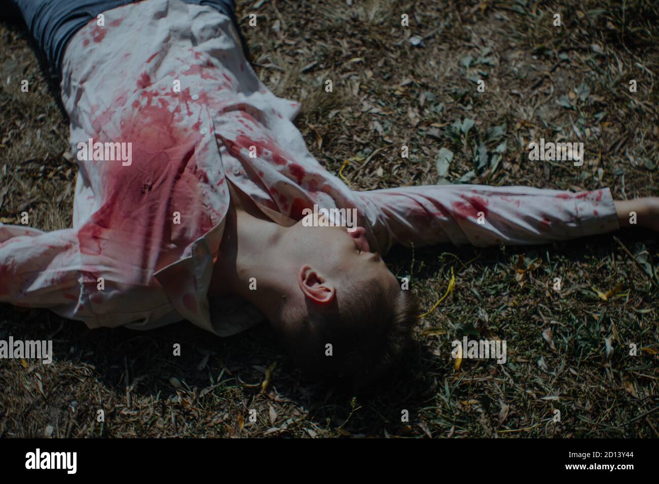 Dead man body lying on the ground in a bloody shirt Stock Photo