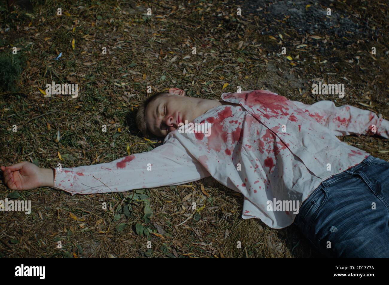 Dead young man is lying on the ground in a bloody shirt Stock Photo