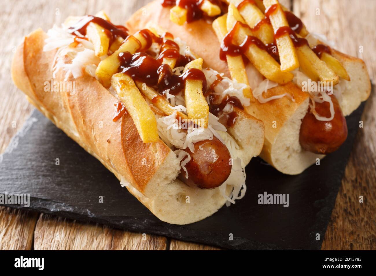 Delicious hot dog polish boy with sausage, cabbage, fries and barbecue sauce close-up on the table. horizontal Stock Photo