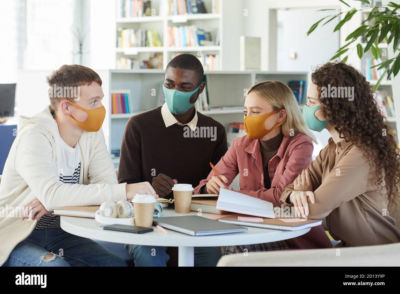 Multi-ethnic group of young people wearing masks while studying ...