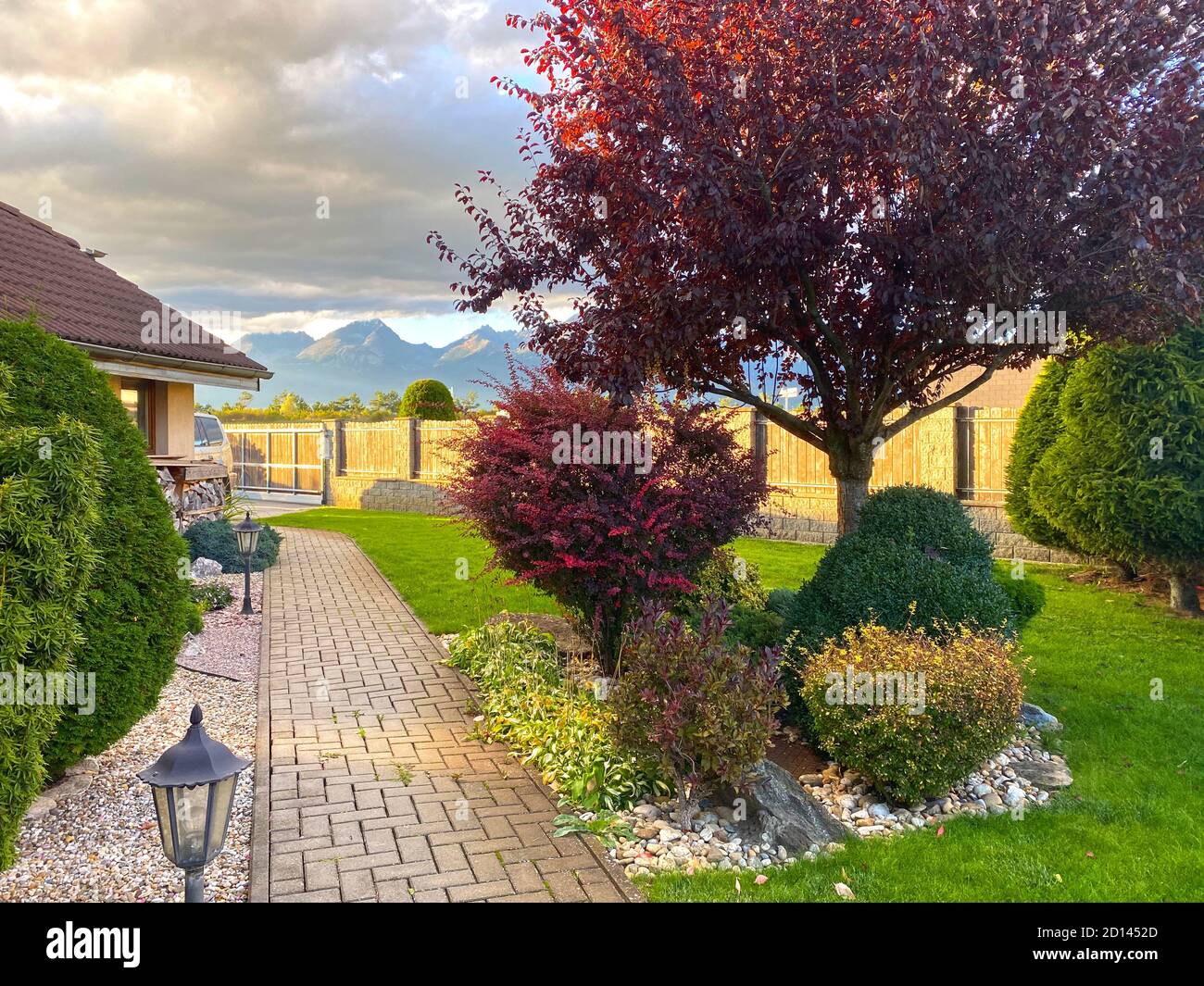 Beautiful autumn/fall colorful plants in the family house garden. Pathway with traditional exterior lamps. View on the mountains. Green lawn. Design Stock Photo
