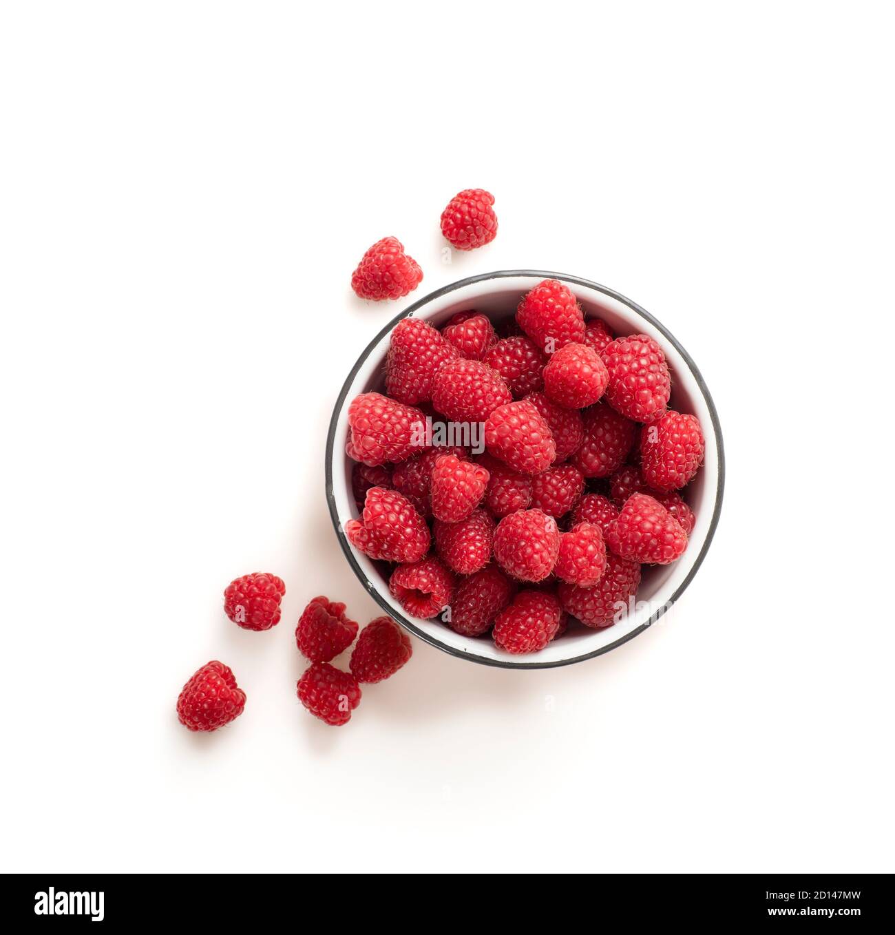 Lots of raspberries in a bowl placed on white, shiny background. Some berries are placed on the surface outsiden the bowl. Picture is shot from above. Stock Photo
