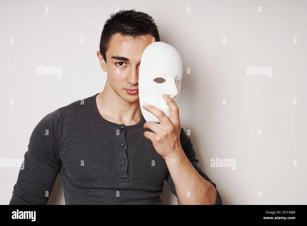 young man taking off white mask revealing face and identity - with copy space Stock Photo