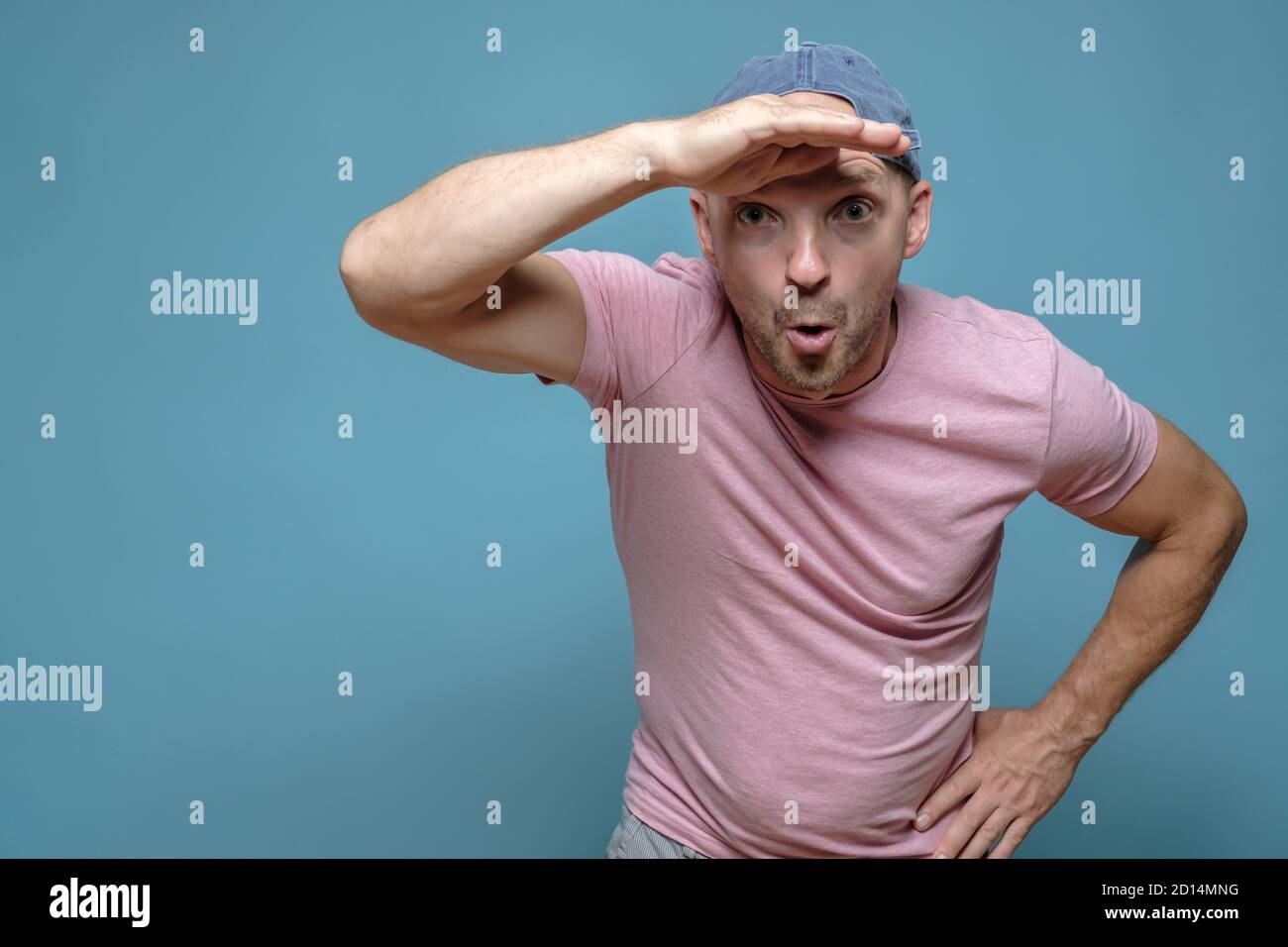 Man is surprised at something, he raised hand to forehead and looks into the distance with a funny expression on face. Copy space.  Stock Photo