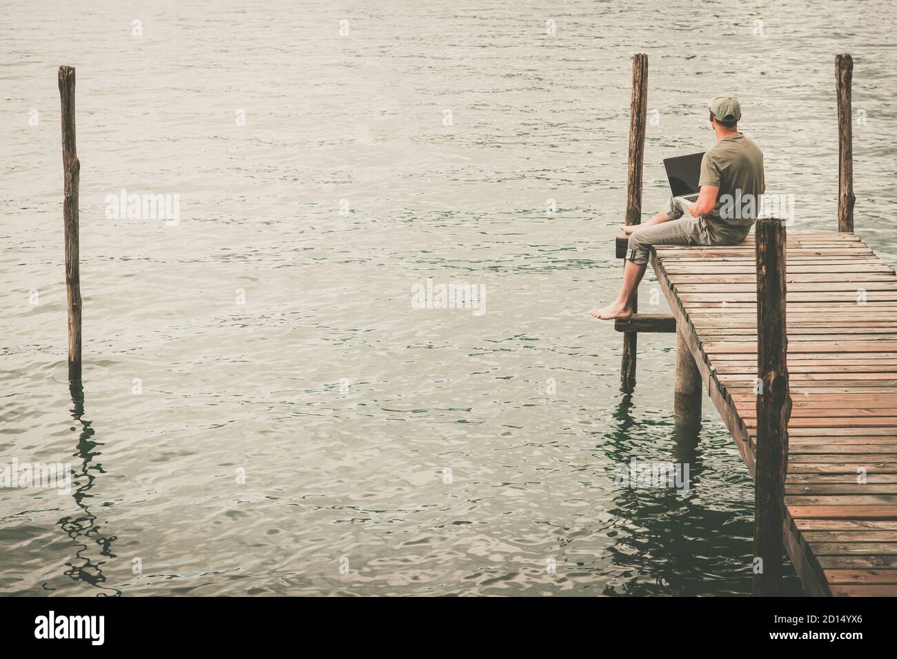 Caucasian Men with Laptop Computer Remotely Working on Wooden Deck and Enjoying Lake View. Remote Place Online Work Theme. Stock Photo
