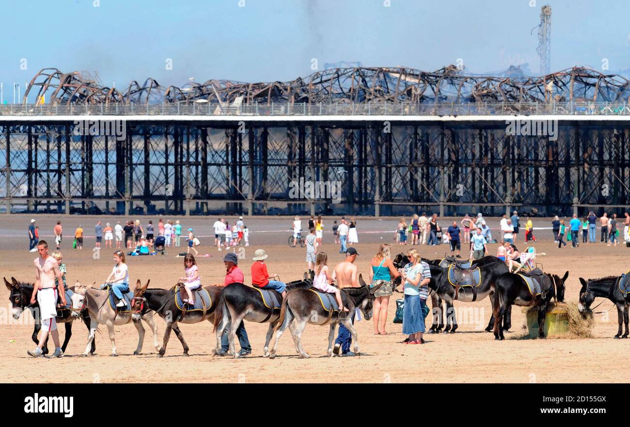 Holiday makers ride donkeys on the beach near the Grand Pier at Weston-Super-Mare in south west England July 28, 2008. Firefighters were called to a large blaze that swept through the historic pier at the Somerset seaside resort of Weston-super-Mare on Monday, police said. Flames and thick black smoke engulfed the structure and could be seen from the M5 motorway, several miles from the coast, a fire brigade spokeswoman said. REUTERS/Toby Melville (BRITAIN) Stock Photo