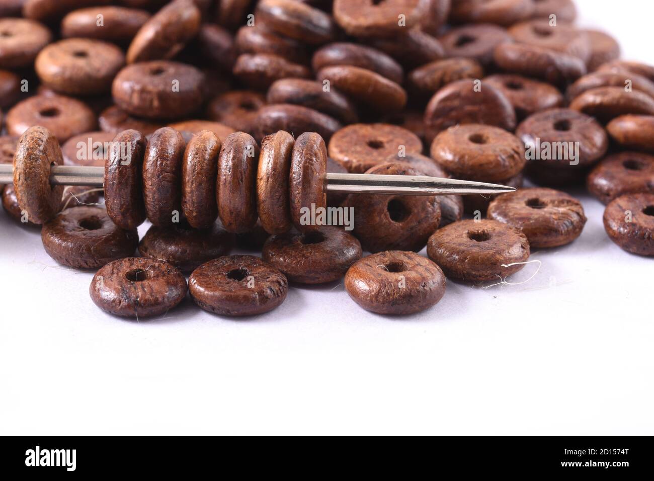 Wooden beads spread on white background with needle. Beads with needle . Close up, macro. Stock Photo