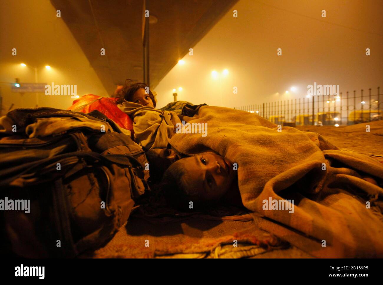 Homeless children use blankets to protect themselves from the cold under a flyover in New Delhi January 21, 2010. The Supreme Court chided the Delhi government to provide night shelters with blankets, water and mobile toilets to all homeless in the capital, local media reported. REUTERS/Reinhard Krause (INDIA - Tags: SOCIETY IMAGES OF THE DAY) Stock Photo