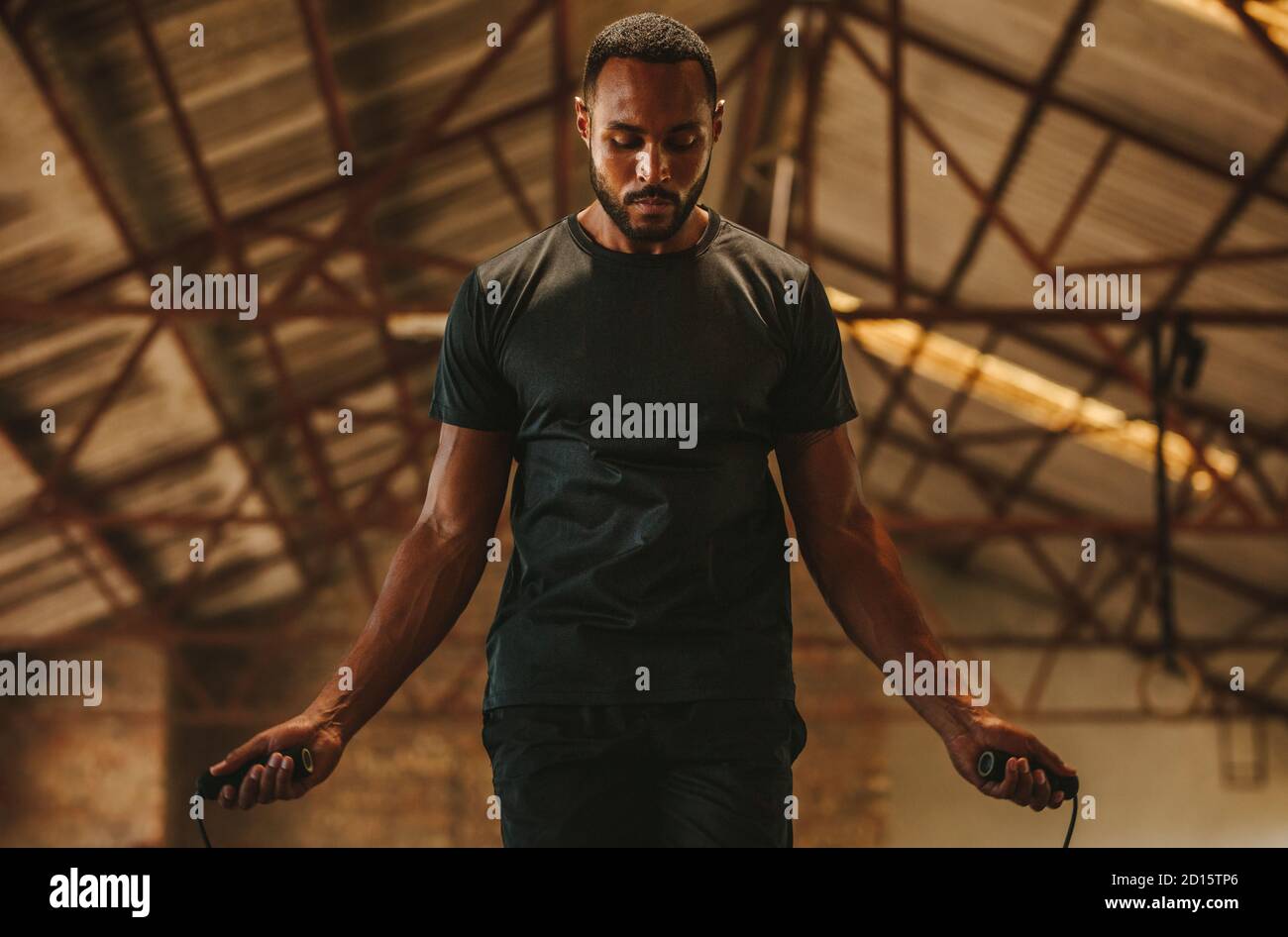 Fitness man with jumping rope in gym at old warehouse. Male exercising with skipping rope at cross workout space. Stock Photo