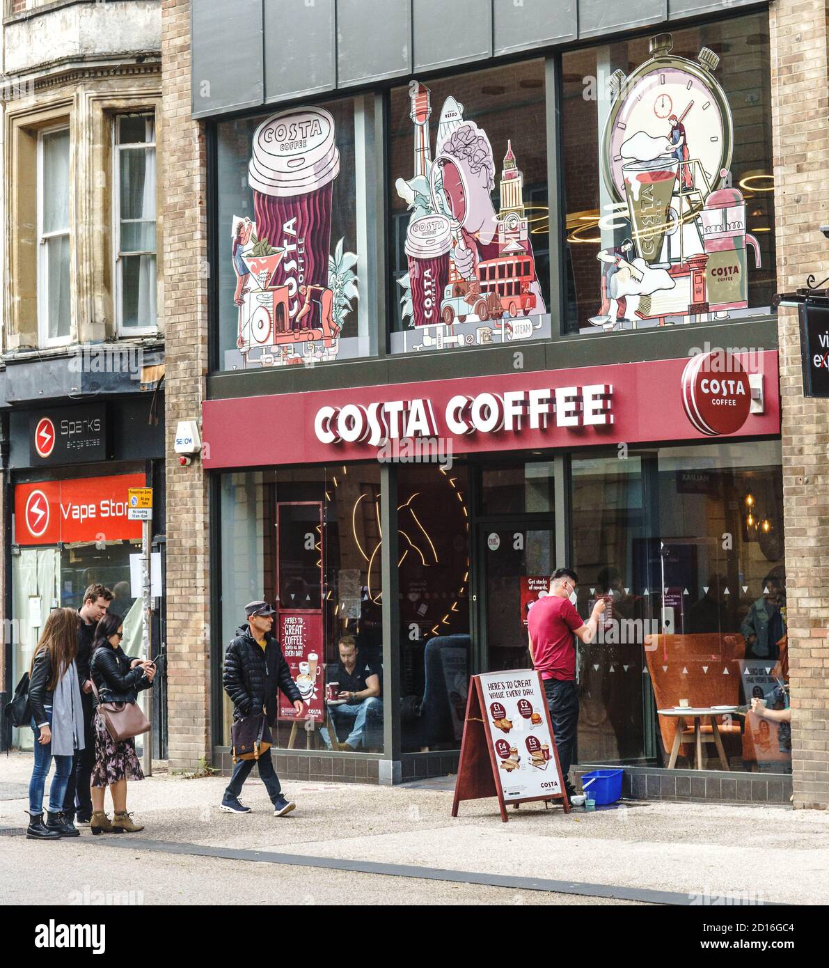 A barista cleans the window at Costa Coffee, Oxford, whilst passers by pause to find their bearings. Stock Photo