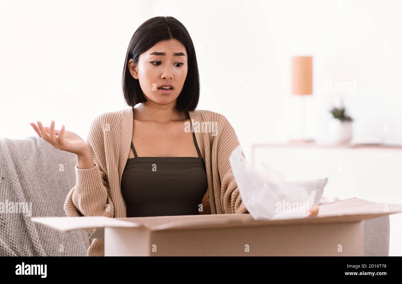 Frustrated young lady unpacking wrong parcel, delivery mistake Stock