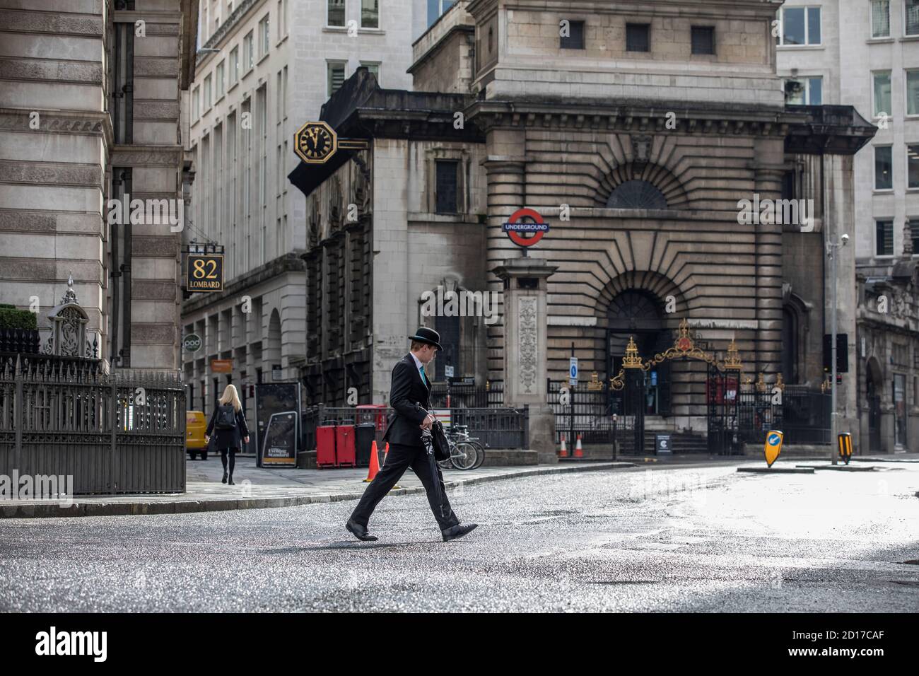 Worker wearing bowler hat carrying an umbrella makes his way across Lombard Street in the financial district of City of London, England, UK Stock Photo