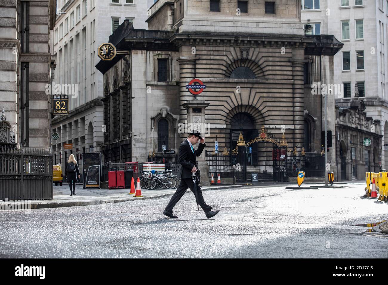 Worker wearing bowler hat carrying an umbrella makes his way across Lombard Street in the financial district of City of London, England, UK Stock Photo
