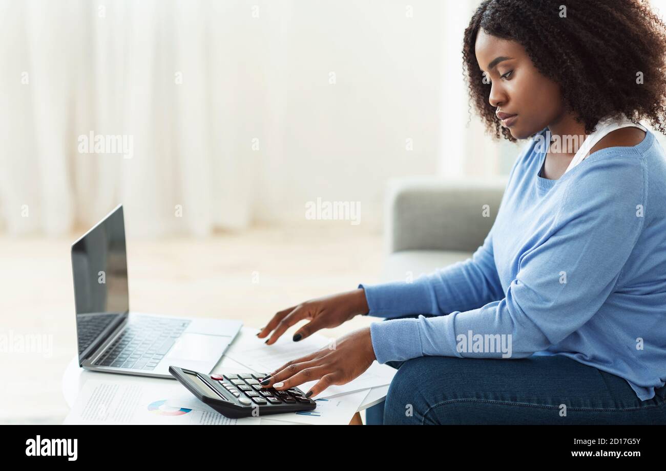 Black woman using calculator and laptop pc at home Stock Photo - Alamy