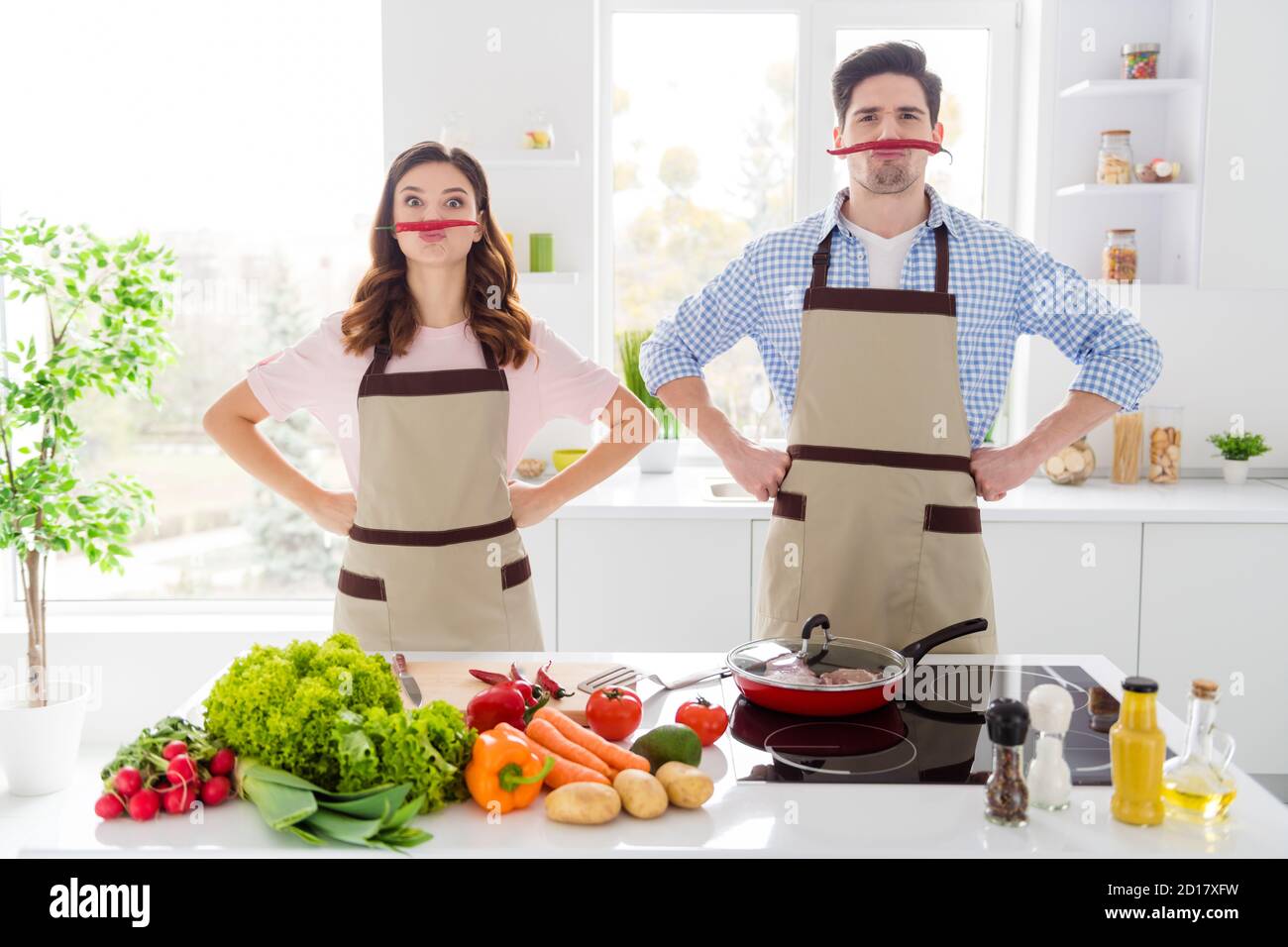 Two funny people enjoy hobby cooking have red hot chilli pepper nose imagine fake mustache comic humor joking prepare dinner in kitchen house indoors Stock Photo