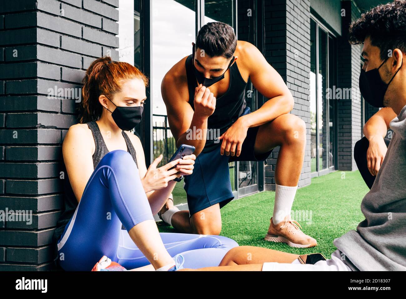 group of young people dressed in sportswear and wearing a face mask using the smartphone when they leave the gym Stock Photo