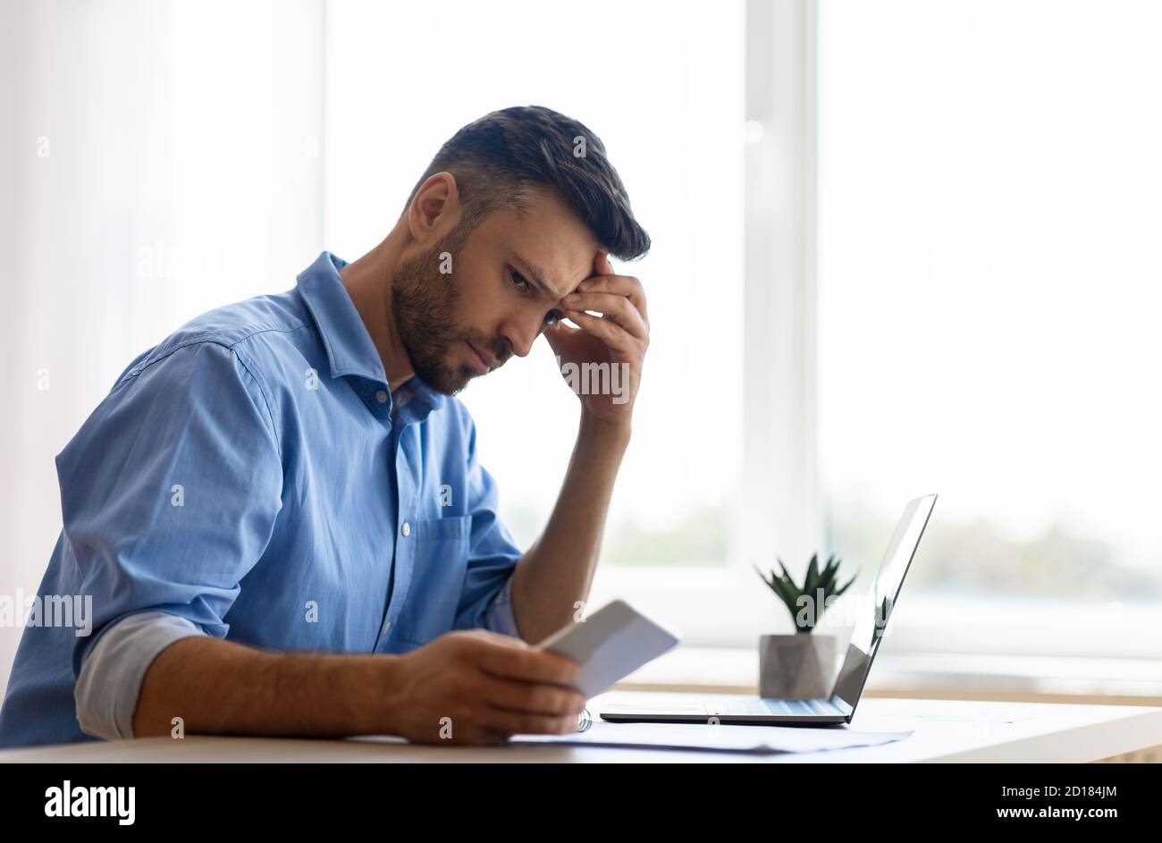 Concerned young businessman looking at smartphone while working in office, waiting message Stock Photo
