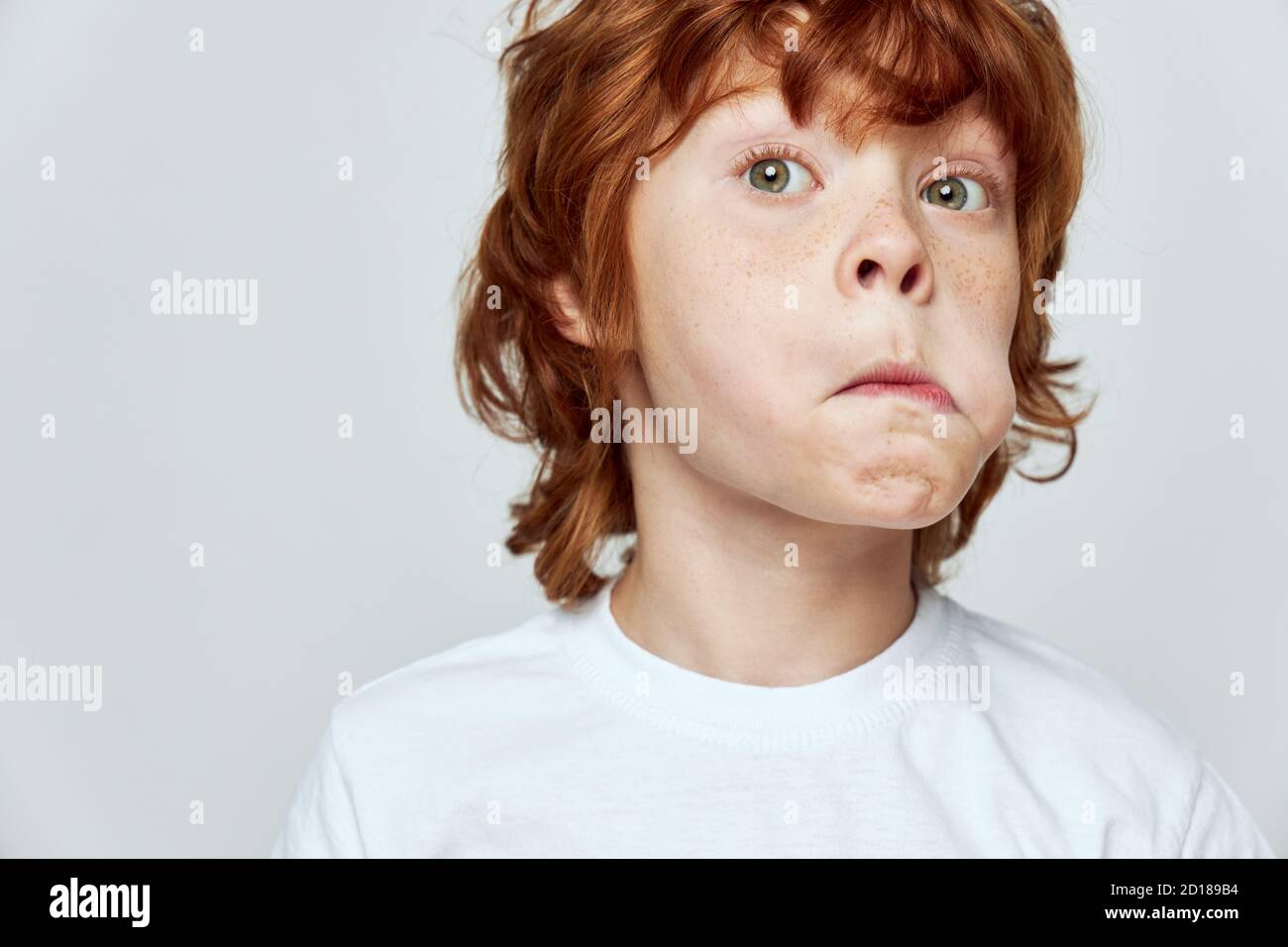 Grimacing red-haired child with puffed out cheek white t-shirt cropped  Stock Photo