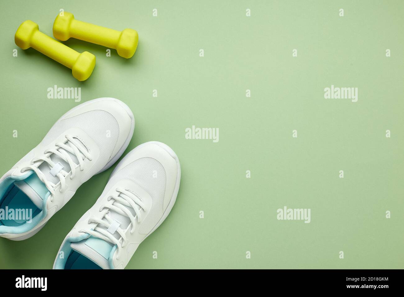 Creative flat lay of sport and fitness equipments. Women's white sneakers and green dumbbells on a light green background. Stock Photo