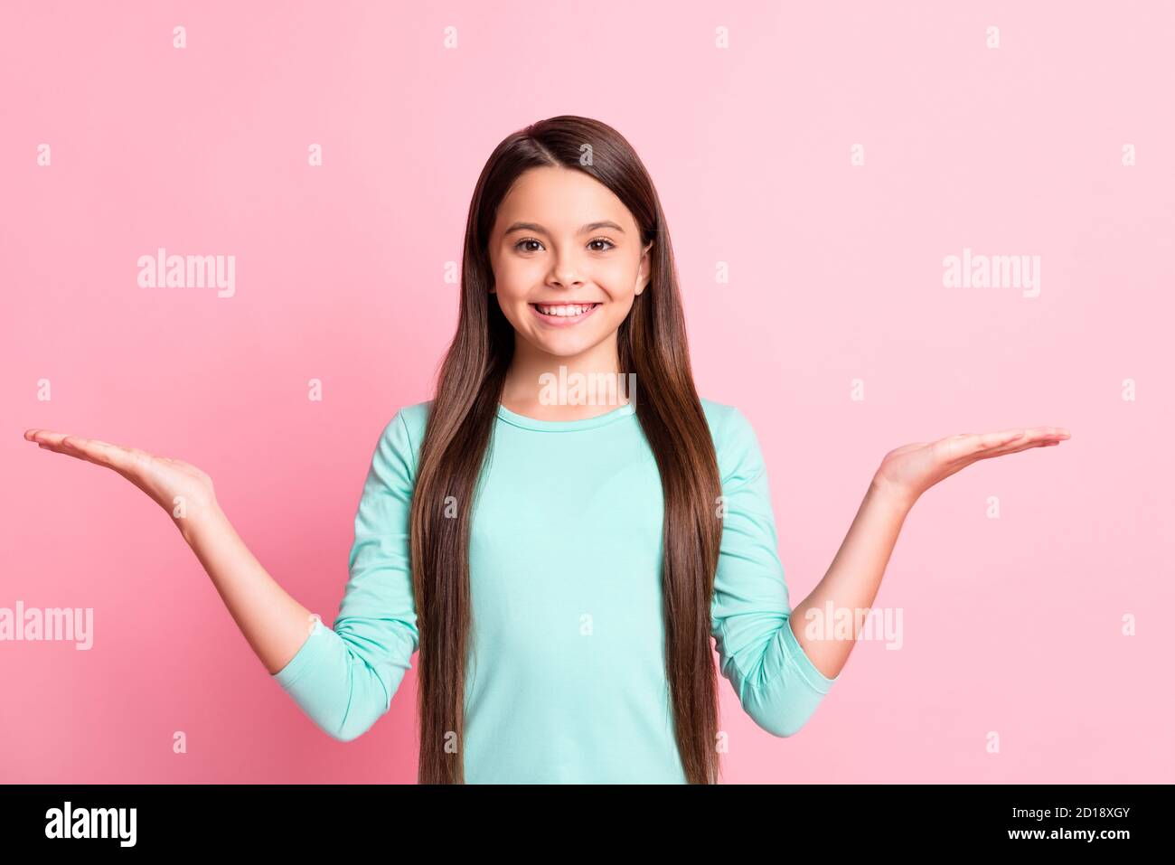 Photo of cheerful lovely sweet little hispanic lady long hairdo raise hands hold empty space propose demonstrate offers smile wear turquoise Stock Photo