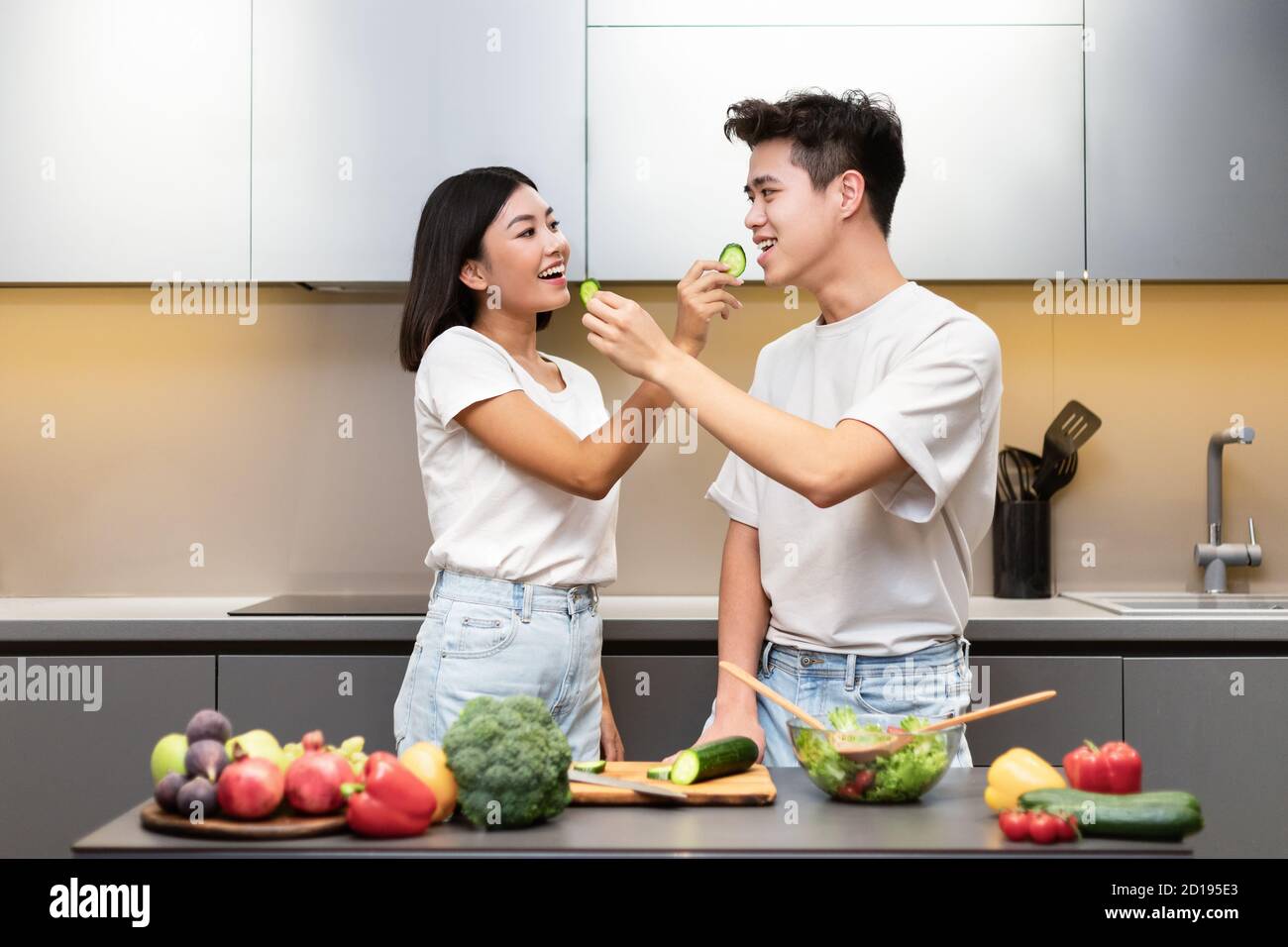 Japanese Couple Cooking Feeding Each Other Tasting Dinner In Kitchen Stock Photo